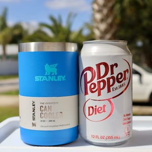 May include: A blue Stanley 10 ounce can cooler with the Stanley logo and the text "The Everyday Can Cooler" and a Diet Dr Pepper can with the text "Dr Pepper Diet Est. 1885" and "12 FL OZ (355 ml)".