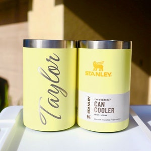 May include: Two yellow Stanley 10 oz. (295 ml) can coolers. One cooler has the word "Taylor" written on it in silver lettering. The other cooler has the Stanley logo and the text "THE EVERYDAY CAN COOLER" on it.