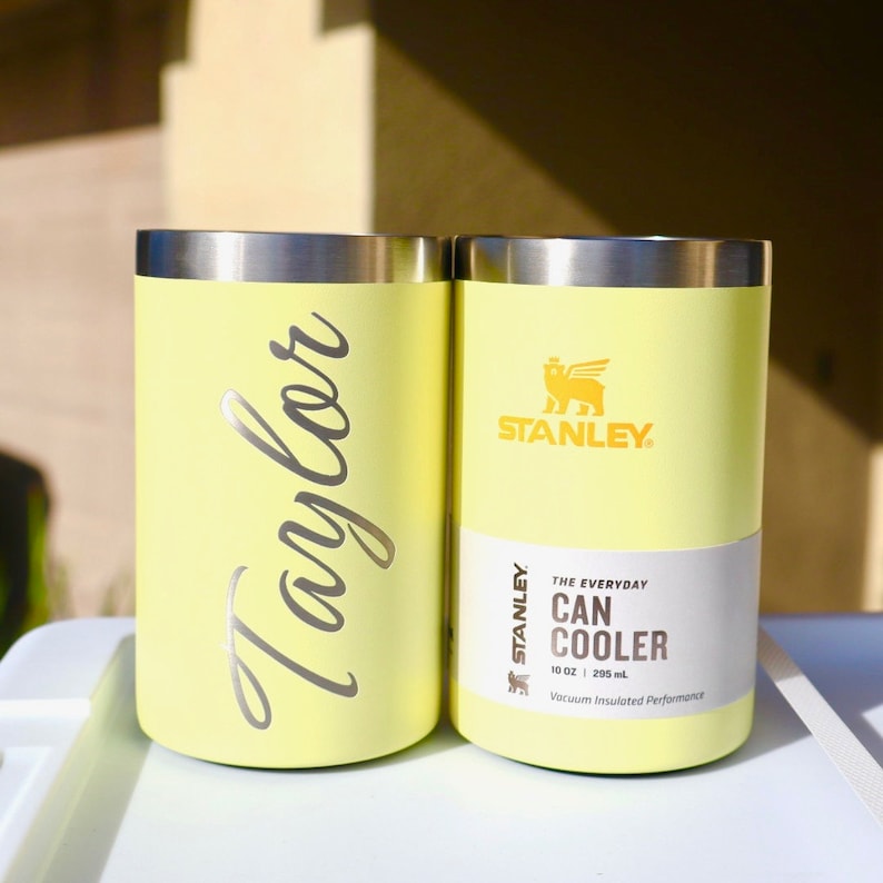 May include: Two yellow Stanley 10 oz. (295 ml) can coolers. One cooler has the word "Taylor" written on it in silver lettering. The other cooler has the Stanley logo and the text "THE EVERYDAY CAN COOLER" on it.