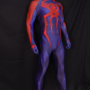 May include: A full-body superhero costume in shades of blue and red. The suit features a high collar and a large red spider emblem on the chest. Red accents are on the shoulders and arms. The costume is displayed on a mannequin.