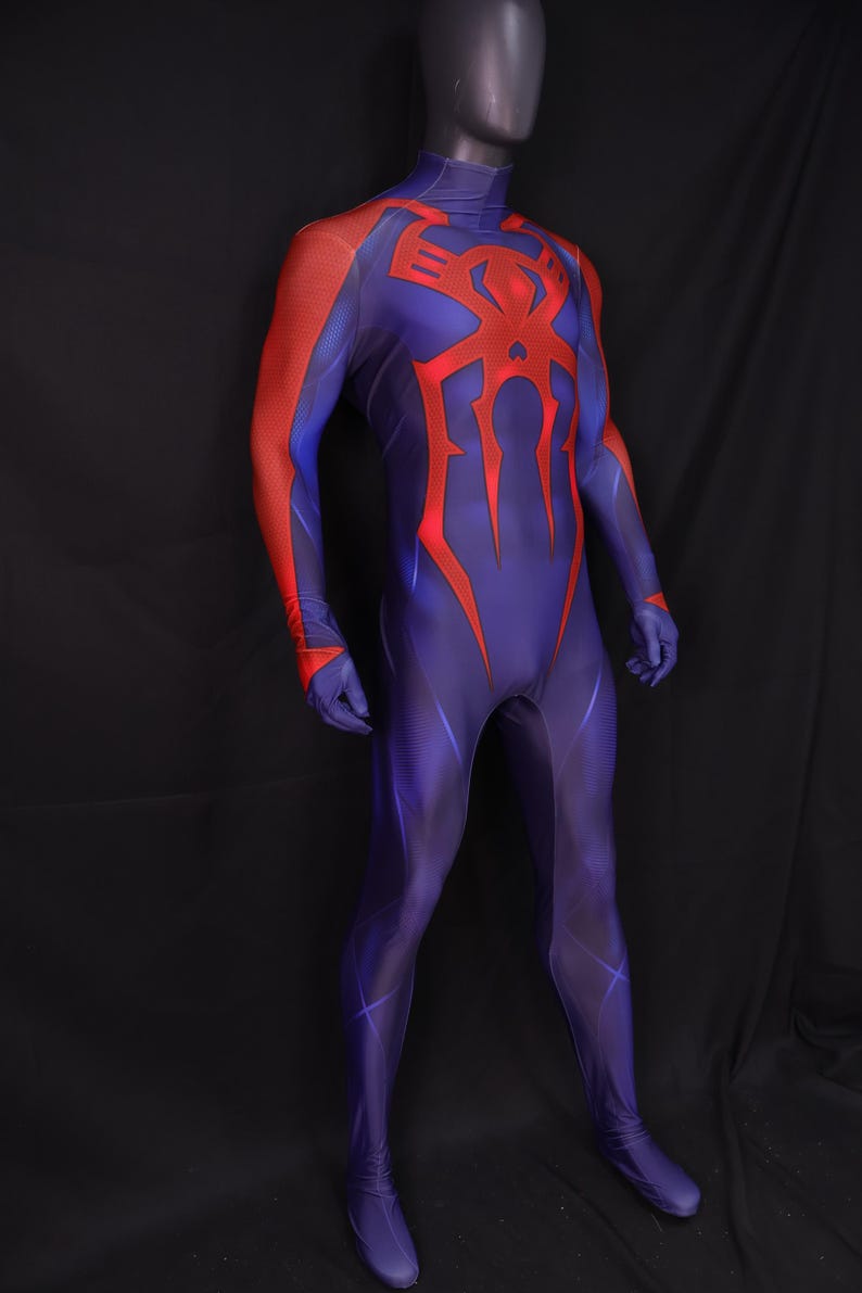 May include: A full-body superhero costume in shades of blue and red. The suit features a high collar and a large red spider emblem on the chest. Red accents are on the shoulders and arms. The costume is displayed on a mannequin.