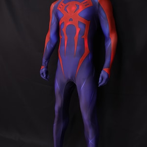 May include: A full-body costume in shades of blue and red, featuring a high collar and a prominent red spider emblem on the chest. The costume has red accents on the arms and a form-fitting design, suitable for cosplay or themed events.