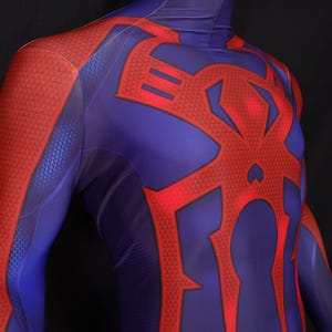 May include: A close-up of a blue and red bodysuit. The suit features a red spider emblem on the back and chest. The arms and shoulders are red with a textured pattern, while the torso is blue.