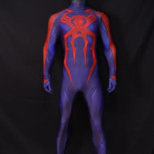 May include: A full-body costume in blue with red accents, displayed on a mannequin. The costume features a red spider emblem on the chest and back, with red detailing on the arms. The suit is form-fitting and covers the entire body.