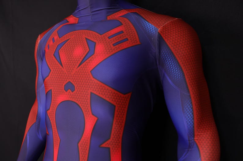 May include: A blue and red superhero costume. The suit features a large red spider emblem on the chest and back, with red accents on the shoulders and arms. The fabric has a textured pattern.