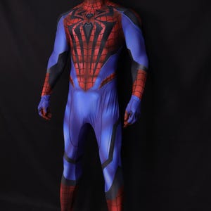 May include: A full-body superhero costume in blue, red, and black, displayed on a mannequin. The costume features a spiderweb design on the chest and a spider emblem. The suit has a form-fitting design with details on the arms and legs.