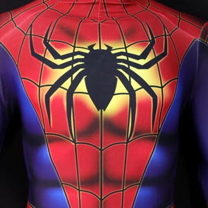 Puede incluir: Un disfraz de Spider-Man rojo, azul y negro. El disfraz presenta un gran emblema de ara&ntilde;a negra en el pecho y la espalda, con un fondo amarillo. El traje tiene un dise&ntilde;o de telara&ntilde;a.