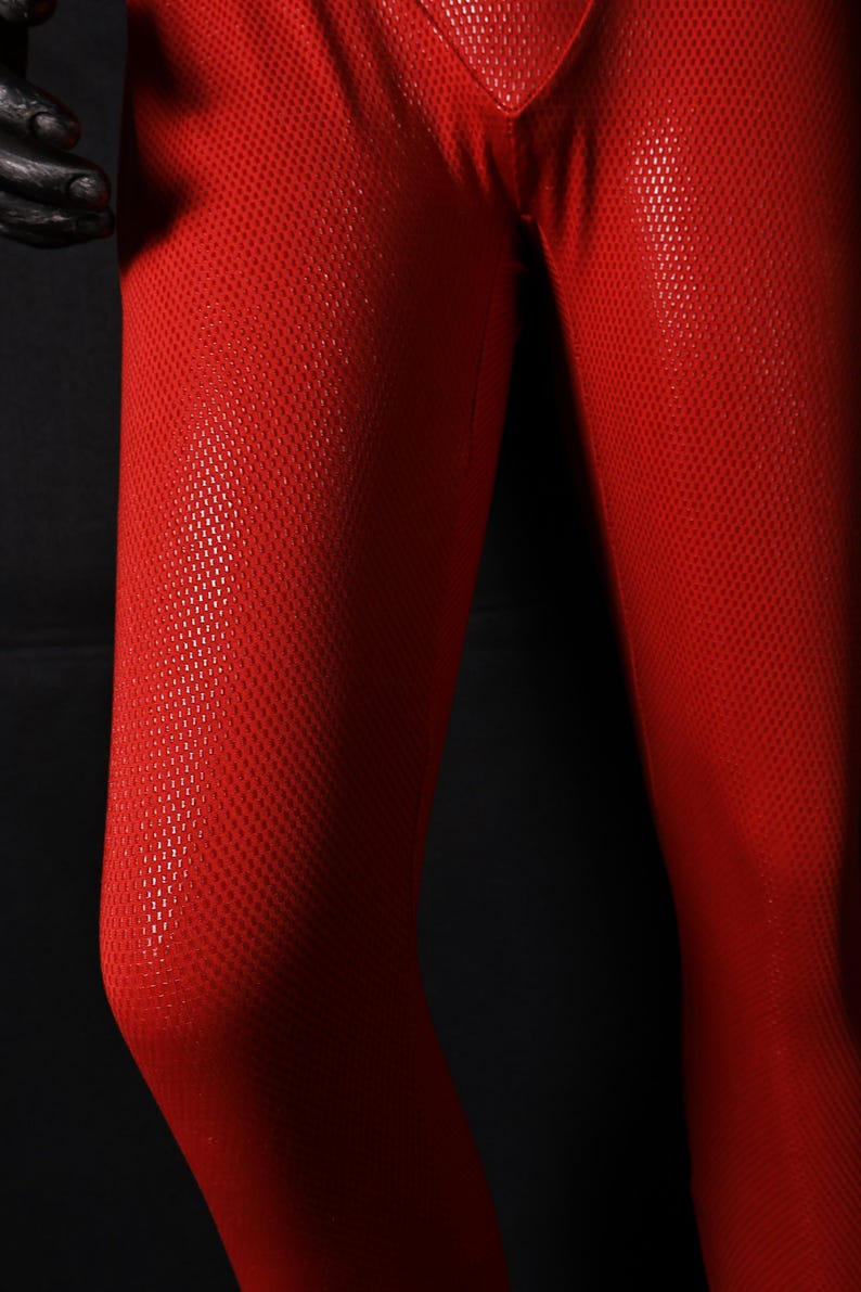 Może przedstawiać: Zbliżenie na czerwone legginsy z teksturowanym, kropkowanym wzorem. Legginsy są wykonane z błyszczącego materiału i wydają się dopasowane. Obraz jest ustawiony na ciemnym tle, podkreślając żywy kolor i fakturę tkaniny.