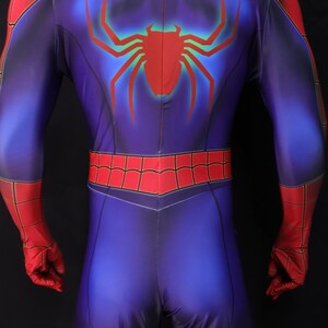 Puede incluir: Un disfraz de superh&eacute;roe azul y rojo con un gran emblema de ara&ntilde;a roja en la espalda. El disfraz presenta un dise&ntilde;o de telara&ntilde;a roja en los hombros y la cintura, con guantes rojos y una capucha roja.