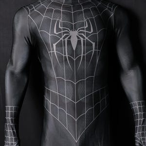 Op de afbeelding: Zwart en grijs Spider-Man-kostuum met een spinnenwebontwerp en een groot spinnenembleem op de borst. Het full-body pak heeft een hoge kraag en bedekt de armen en handen. Het kostuum wordt op een mannequin getoond.