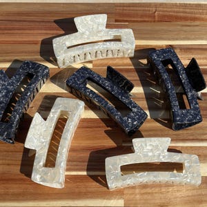 May include: Five hair clips, two are black with a marbled pattern and three are white with a marbled pattern.