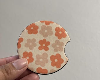 May include: A round, white car coaster with a pattern of orange and pink flowers. The coaster is made of a soft, absorbent material.