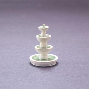 May include: A miniature, three-tiered fountain with a white exterior and green accents. The fountain has a classic design, with each tier slightly smaller than the one below. The base is a wide, shallow dish, also with green detailing.