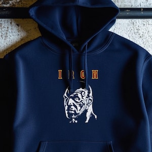 May include: A navy blue hooded sweatshirt with a white graphic of a man's face with the word "IRON" printed above it.