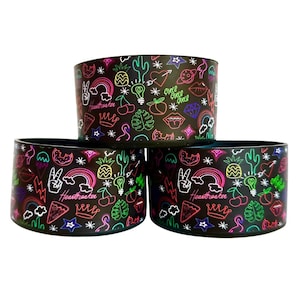 May include: Three black reusable coffee cup sleeves with a neon pink, green, and yellow graphic print. The print features a variety of designs including hearts, stars, rainbows, cherries, pineapples, and the words "Heartbreaker" and "Girls Girls Girls".