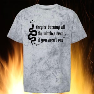 May include: A gray marbled t-shirt with the text "they're burning all the witches even if you aren't one" in black gothic font. A black snake and star graphic is on the left side of the text.