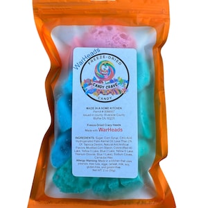May include: A bag of freeze-dried WarHeads Crazy Heads candy. The bag is orange and clear, and the candy is blue, pink, and green. The bag has a label that says "WarHeads Freeze-Dried Candy Crave Candy" and "Made in a Home Kitchen".