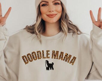 May include: A beige sweatshirt with the text "Doodle Mama" in leopard print letters. A black doodle dog silhouette is below the text.