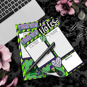 Könnte beinhalten: Ein Stapel bunter Notizblöcke mit dem Text "CANNA MOM" und "notes". Die Notizblöcke haben ein grünes, lila und weißes Design mit Cannabisblatt-Illustrationen und den Sätzen "High Enough To Do Today" und "Not High Enough - Do Tomorrow". Ein schwarzer Stift liegt auf den Notizblöcken.
