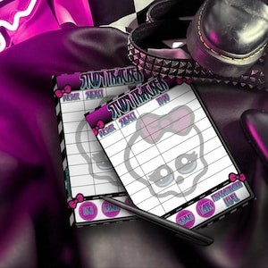 May include: Two white study tracker notepads with a skull graphic and the text "Study Tracker". The notepads have pink bow accents and a black pen. The background includes black shoes and a studded belt.