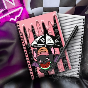 May include: A spiral-bound notebook featuring a pink dripping top edge and a black and pink striped background with skull patterns. A cartoon bat wearing a hat that says SUMMER WEEN holds a watermelon slice under a black and white skull umbrella.