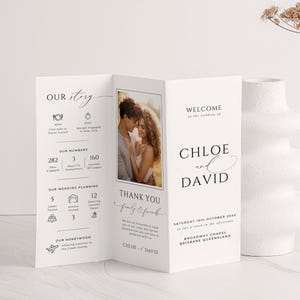 Könnte beinhalten: Ein weißes Hochzeitsprogramm mit einem Foto eines Paares, den Namen "Chloe und David" und Hochzeitsdetails. Das Programm enthält den Text "Our Story", "Our Numbers" und "Thank You". Eine weiße Vase und eine Trockenblume befinden sich im Hintergrund.