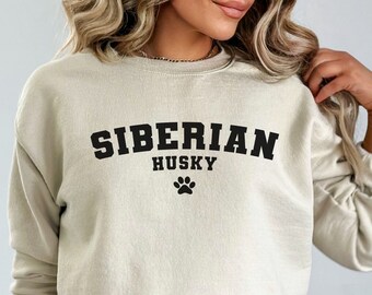 May include: A beige sweatshirt with the words "SIBERIAN HUSKY" in black block letters, with "HUSKY" below "SIBERIAN". A black paw print is below "HUSKY". The sweatshirt has long sleeves.