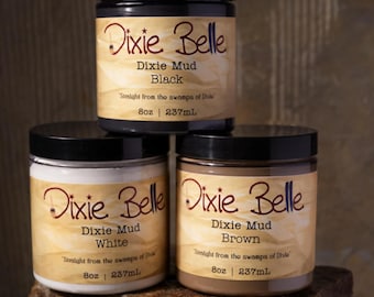 May include: Three cylindrical jars of Dixie Belle Dixie Mud in black, white, and brown. Each jar features a black lid and a tan label with the text Dixie Belle, Dixie Mud, and Straight from the swamps of Dixie, noting 8oz | 237mL capacity.