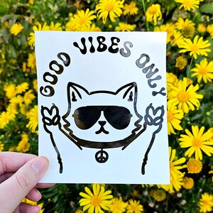 May include: Black and white sticker with a cat wearing sunglasses and peace sign necklace. The text "Good Vibes Only" is written in a circle around the cat.
