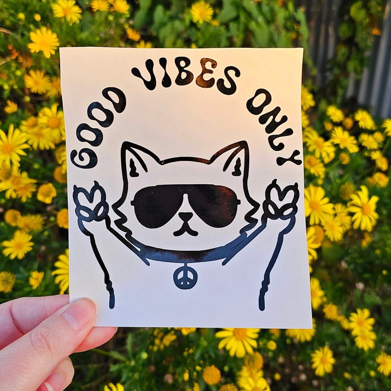 May include: White sticker with a black outline of a cat wearing sunglasses and peace sign necklace. The text "Good Vibes Only" is written in a curved font around the cat.