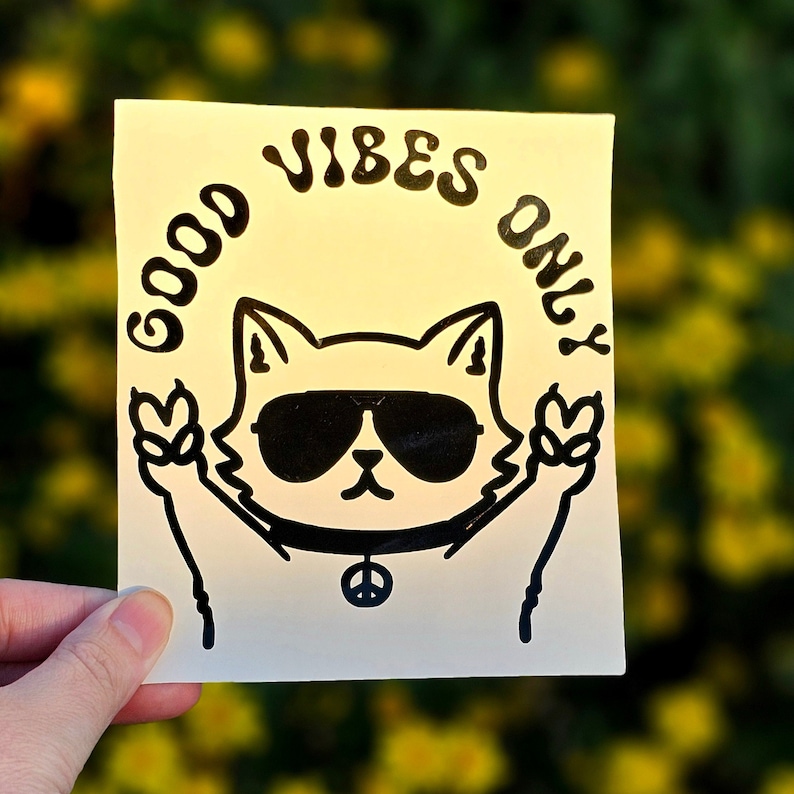 May include: White sticker with a black outline of a cat wearing sunglasses and peace sign necklace. The text "Good Vibes Only" is written in a circle around the cat.