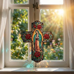 Könnte beinhalten: Ein kreuzförmiger Buntglas-Sonnenfänger mit einer zentralen Darstellung der Jungfrau von Guadalupe in einem blaugrünen und rosafarbenen Gewand, umgeben von roten Rosen und grünen Blättern, aufgehängt an einer goldfarbenen Metallkette vor einem Fenster.