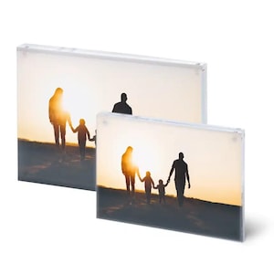 Könnte beinhalten: Zwei rechteckige Fotorahmen mit einer Familiensilhouette, die auf den Sonnenuntergang zugeht. Die Rahmen sind transparent, so dass das Bild von beiden Seiten sichtbar ist. Das Bild zeigt eine vierköpfige Familie, die Händchen hält.
