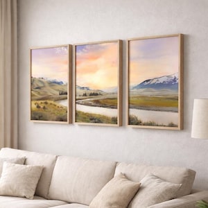 Könnte beinhalten: Drei gerahmte Landschaftsbilder, die einen Fluss zeigen, der sich durch ein Tal mit Bergen im Hintergrund schlängelt. Das Kunstwerk weist eine warme Farbpalette mit Orange-, Gelb- und Blautönen sowie Holzrahmen auf. Die Gemälde werden über einem beigen Sofa ausgestellt.