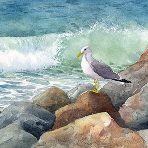 Watercolor painting of a seagull standing on rocks near the ocean. The bird has gray wings, a white body, and a yellow beak and feet. The background features a crashing wave and blue-green water.
