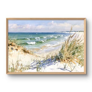 May include: A framed watercolour painting depicting a coastal scene with white sand dunes, tall golden beach grass, and turquoise ocean waves under a light blue sky with soft clouds. The artwork is enclosed in a simple light wood frame.