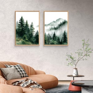 May include: Two framed watercolor prints of forest scenes. One features tall evergreen trees, the other a mountain range with trees shrouded in mist. The artwork has a natural wood frame and a white background.