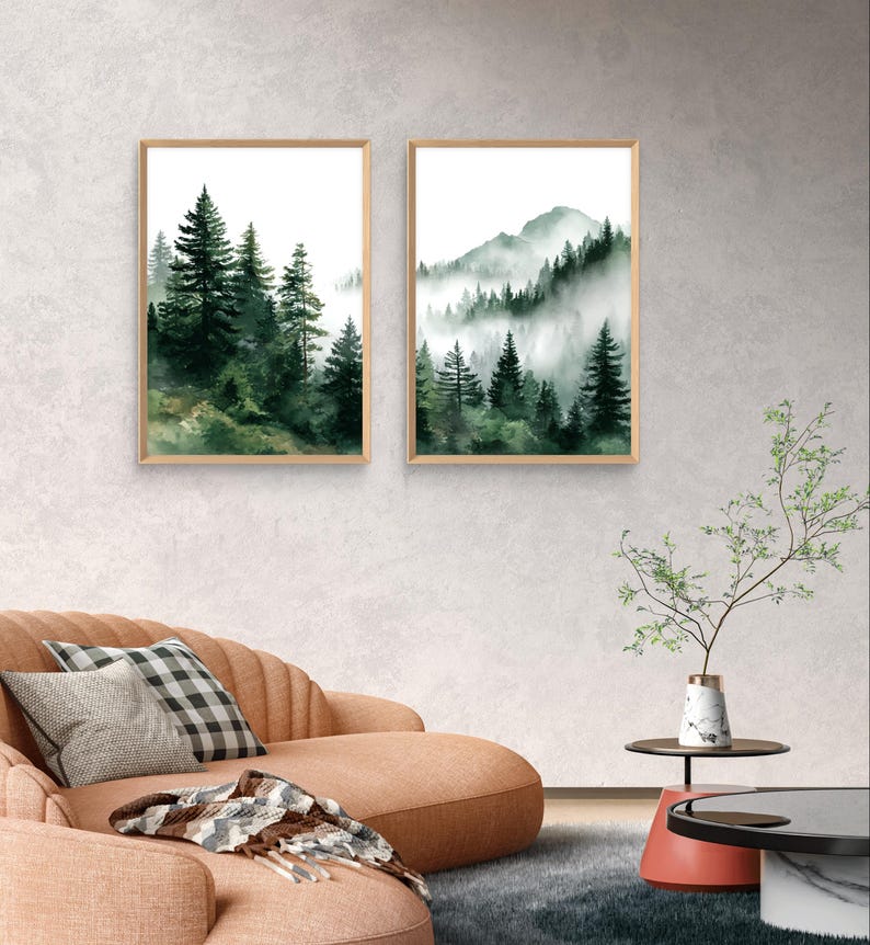 May include: Two framed watercolor prints of forest scenes. One features tall evergreen trees, the other a mountain range with trees shrouded in mist. The artwork has a natural wood frame and a white background.