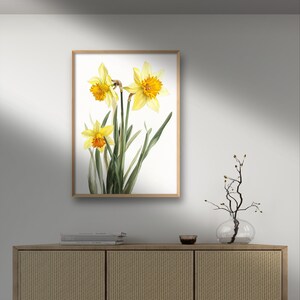 May include: A framed watercolor painting of three yellow daffodils with orange centers on a white background.
