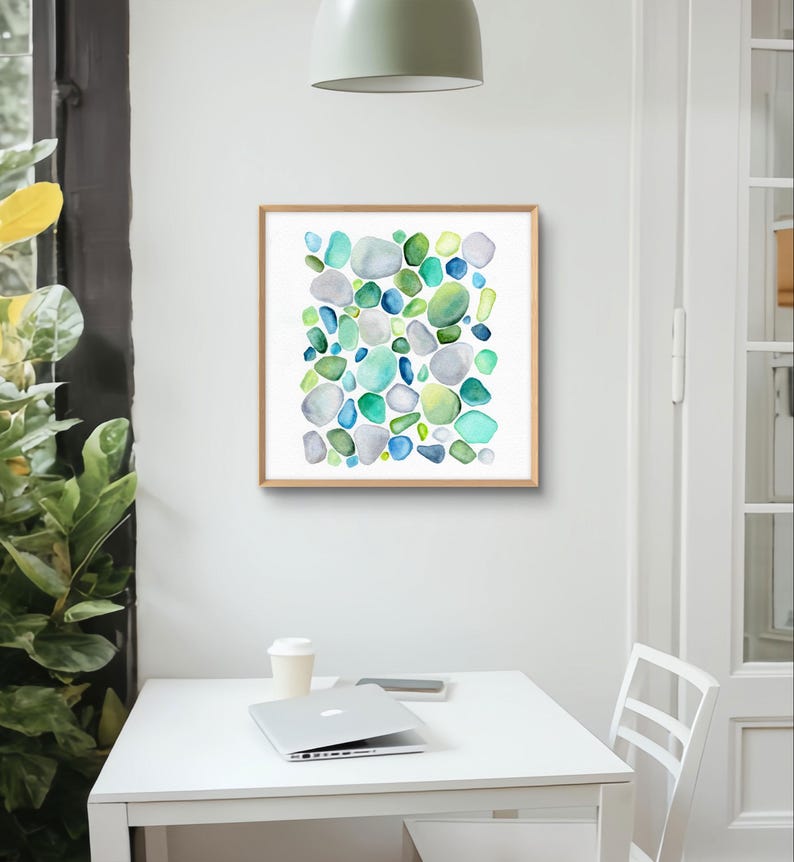 Puede incluir: Una impresi&oacute;n en acuarela enmarcada con un dise&ntilde;o abstracto de formas redondeadas y coloridas en tonos azules, verdes y grises. La obra de arte se muestra en un marco de madera clara. La impresi&oacute;n se muestra en una habitaci&oacute;n con una mesa blanca y un port&aacute;til.