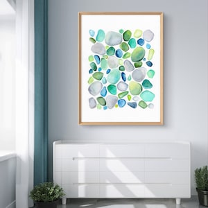 Puede incluir: Una impresi&oacute;n en acuarela enmarcada que presenta un dise&ntilde;o abstracto de piedras redondeadas y coloridas. Las piedras son en tonos de azul, verde y gris, sobre un fondo blanco. El marco es de madera clara. La obra de arte se exhibe sobre una c&oacute;moda blanca.