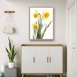 May include: A framed print of a watercolor painting of yellow daffodils with green leaves on a white background.