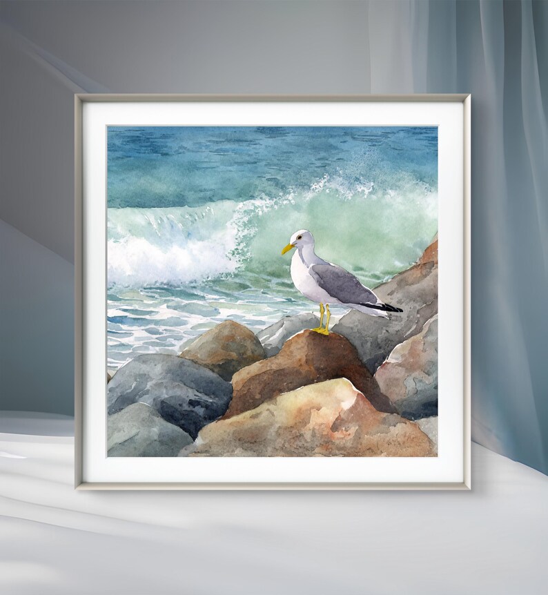 May include: Watercolor painting of a seagull perched on rocks at the ocean's edge. The artwork features a white and gray seagull with a yellow beak and legs, set against a backdrop of crashing waves and a blue-green sea. The painting is framed.