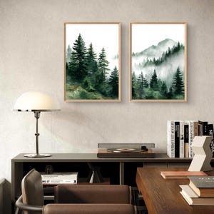 May include: Two framed watercolor prints of forest scenes. One depicts tall evergreen trees, the other a mountain range with trees shrouded in mist. Both are in light wood frames, creating a natural aesthetic.