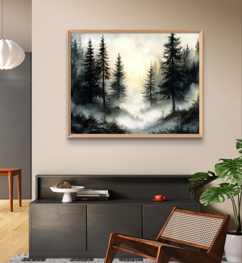 May include: A framed watercolor painting of a misty forest scene. The artwork features tall, dark evergreen trees silhouetted against a bright, hazy sky. The painting is in a natural wood frame and hangs above a dark gray cabinet.