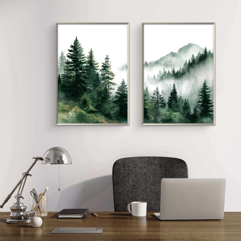 May include: Two framed watercolor prints of forest scenes. One depicts a dense forest of green trees, the other a mountain range with trees and fog. Both are in silver frames, creating a serene, natural aesthetic.