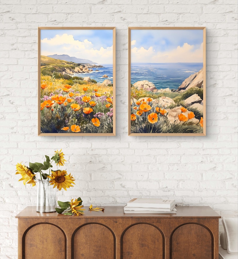 May include: Two framed watercolor paintings of a coastal landscape with orange wildflowers in the foreground and a blue ocean in the background.
