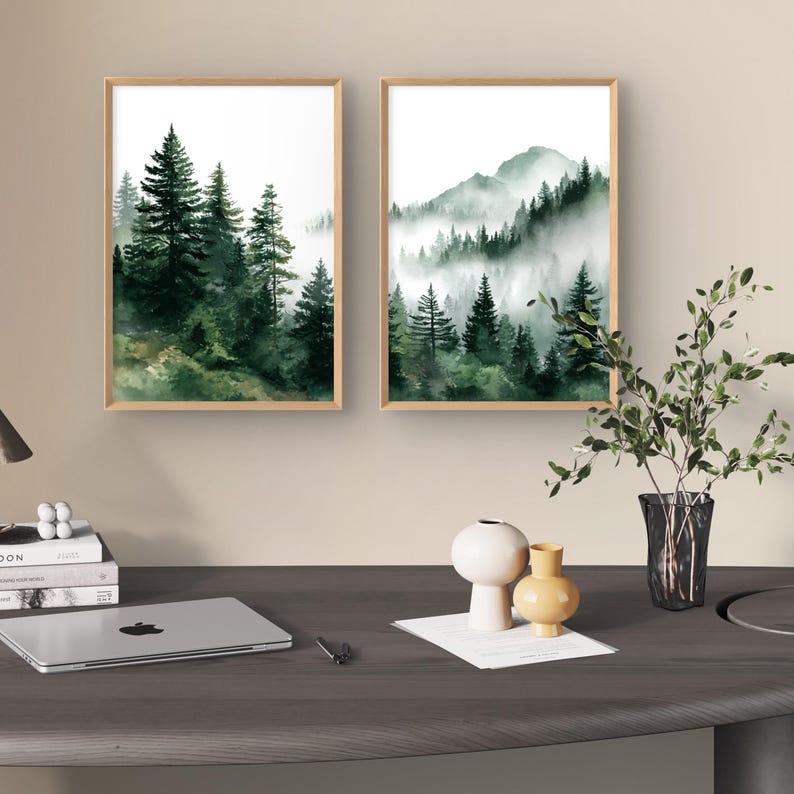 May include: Two framed watercolor prints depict forest scenes. One shows tall evergreen trees, the other a mountain range with trees shrouded in mist. The frames are light brown, and the artwork features shades of green and white.