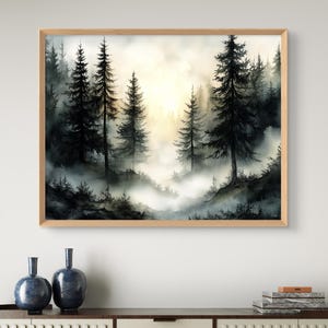 May include: A framed watercolor painting of a misty forest scene. Tall, dark evergreen trees dominate the foreground, with a soft, golden light filtering through the fog in the background. The artwork is displayed in a light brown wooden frame.