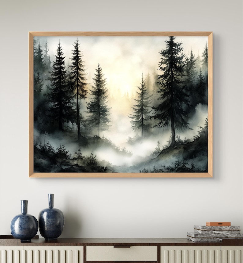 May include: A framed watercolor painting of a misty forest scene. Tall, dark evergreen trees dominate the foreground, with a soft, golden light filtering through the fog in the background. The artwork is displayed in a light brown wooden frame.